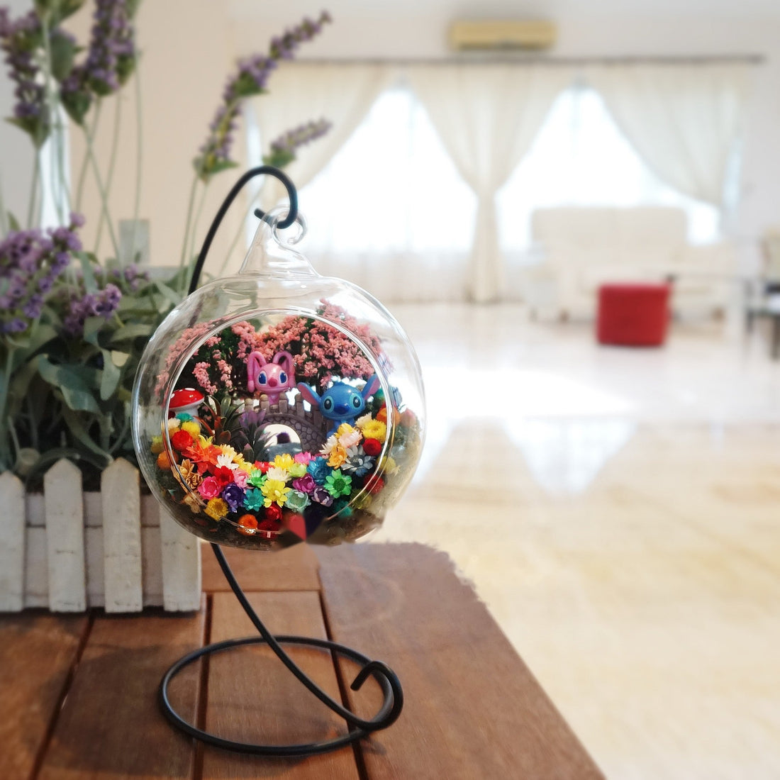 Round glass terrarium with a pair of blue creature figurines among preserved flowers