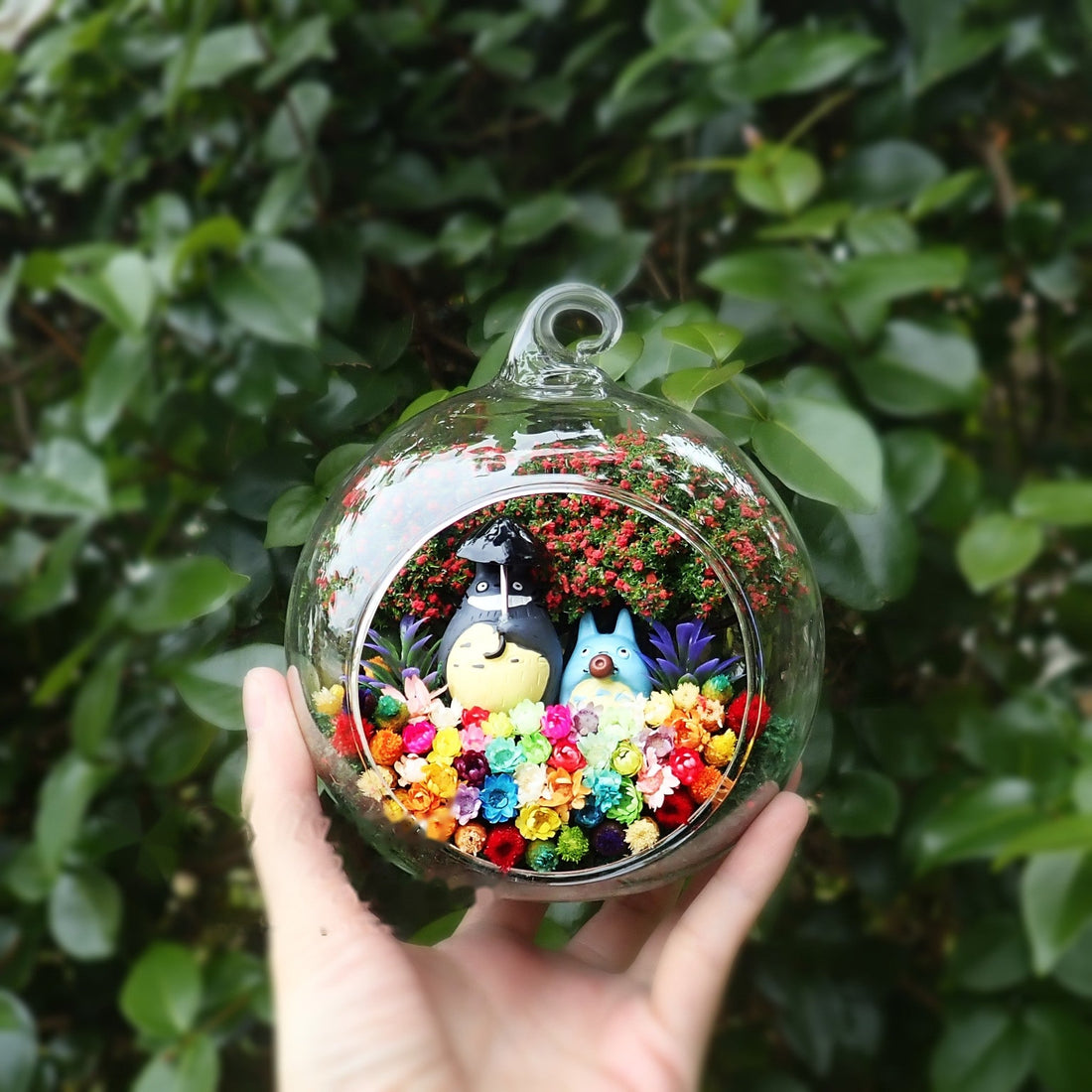 Round glass terrarium with grey and blue figurines among preserved flowers