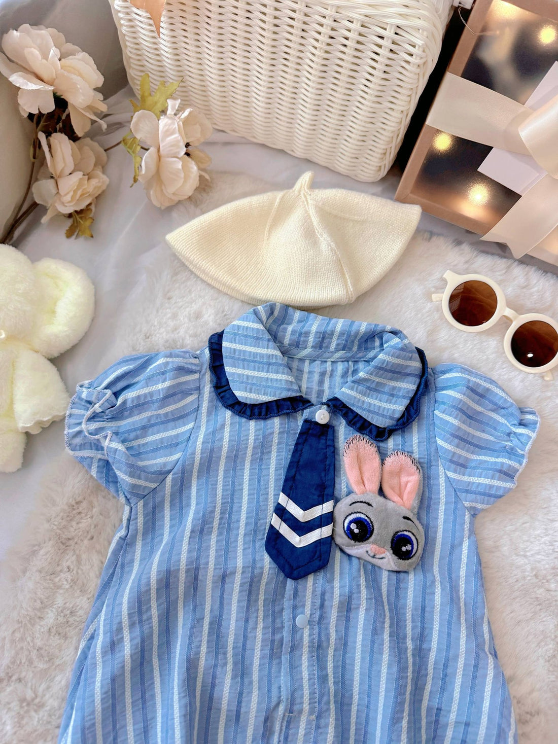 Judy Bunny baby outfit flat lay – blue striped romper with tie and bunny badge