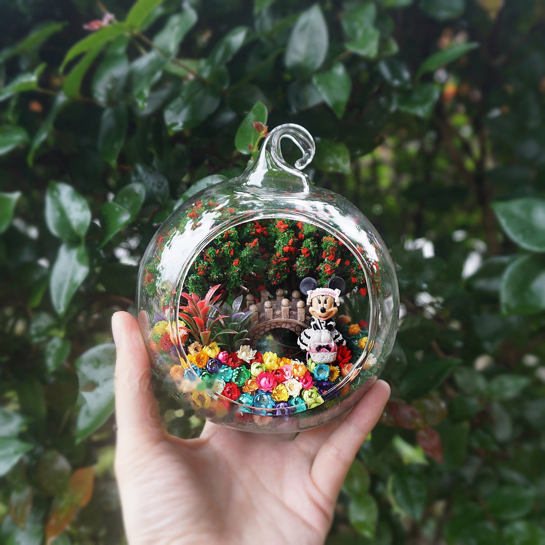Round glass terrarium with a mouse figurine in a dress among preserved flowers
