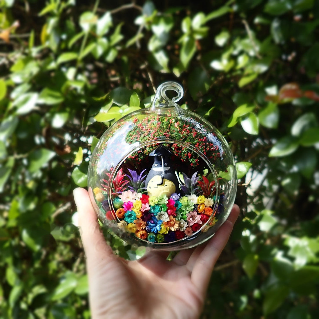 Terrarium kaca bulat dengan patung bulat kelabu di antara bunga awet