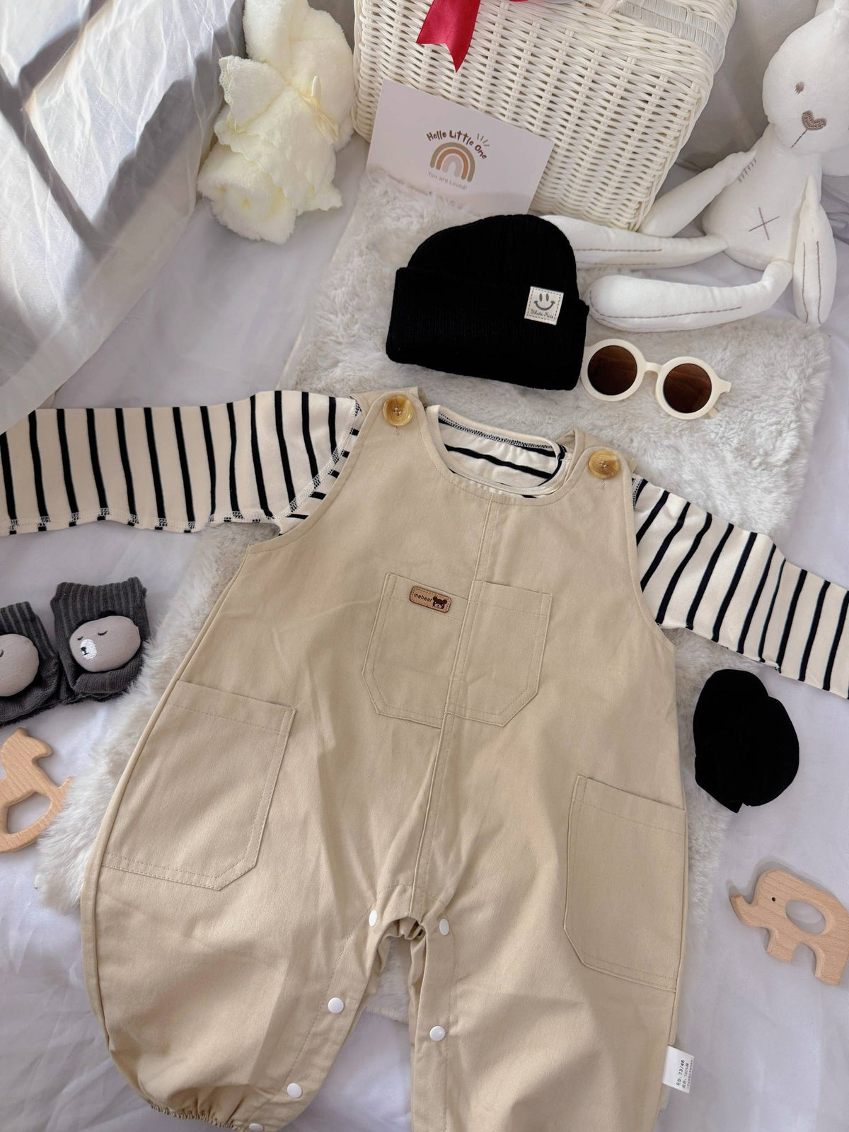 Tiny Trendsetter baby outfit flat lay – khaki overalls with striped top and black beanie