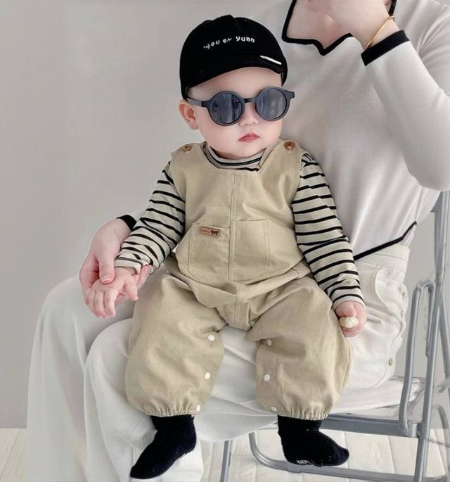 Baby wearing the Tiny Trendsetter khaki overalls with striped top and black beanie