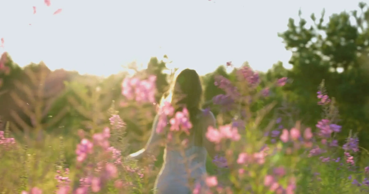 Woman walking through pink wildflowers at golden hour