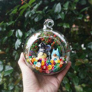 Terrarium kaca bulat dengan patung kelabu dan biru di sebelah papan hentian bas di antara bunga awet