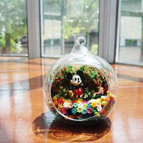 Terrarium kaca bulat dengan patung tikus besar di antara bunga awet
