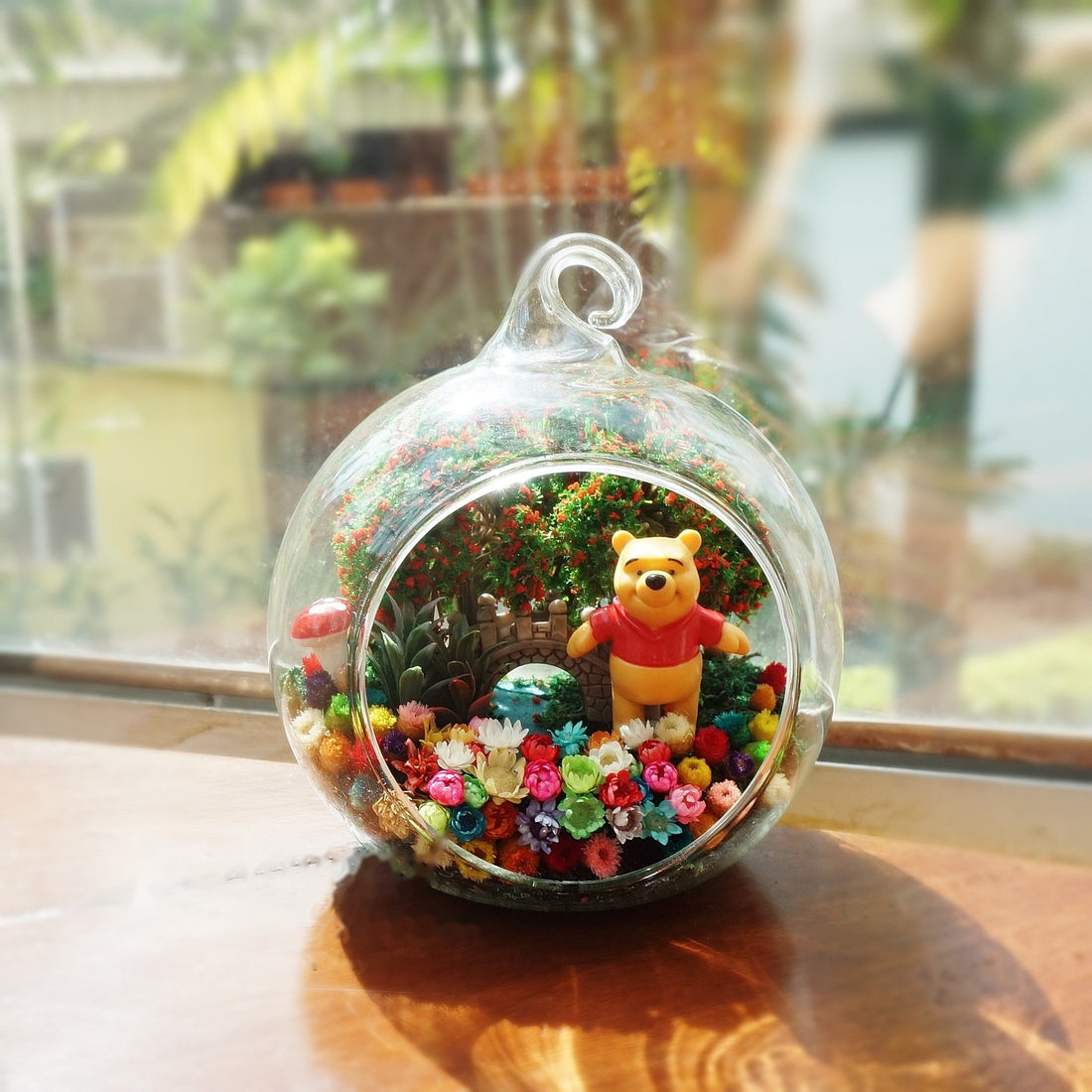 Round glass terrarium with a large yellow bear figurine among preserved flowers