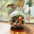 Round glass terrarium with a large yellow bear figurine among preserved flowers