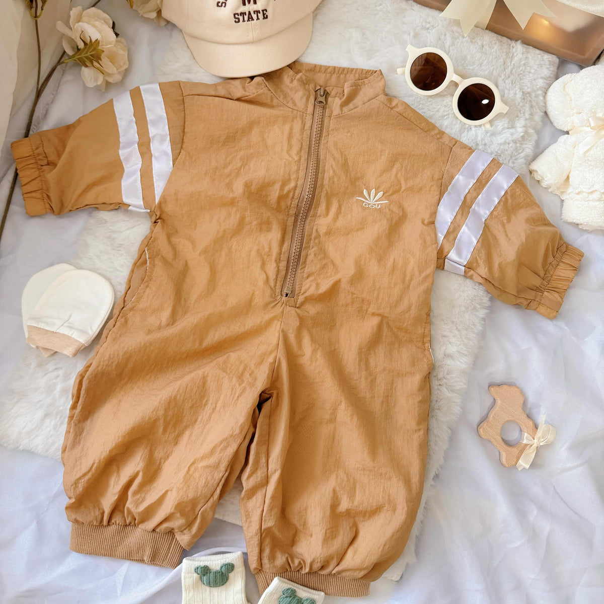 Flat lay view of Little Explorer baby hamper – sporty zip-up romper, sunglasses, matching hat, baby socks, towel bear and mittens