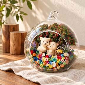 Two Bears preserved flower terrarium on ivory linen over a wooden table, with wooden ornaments and green leaves in the background