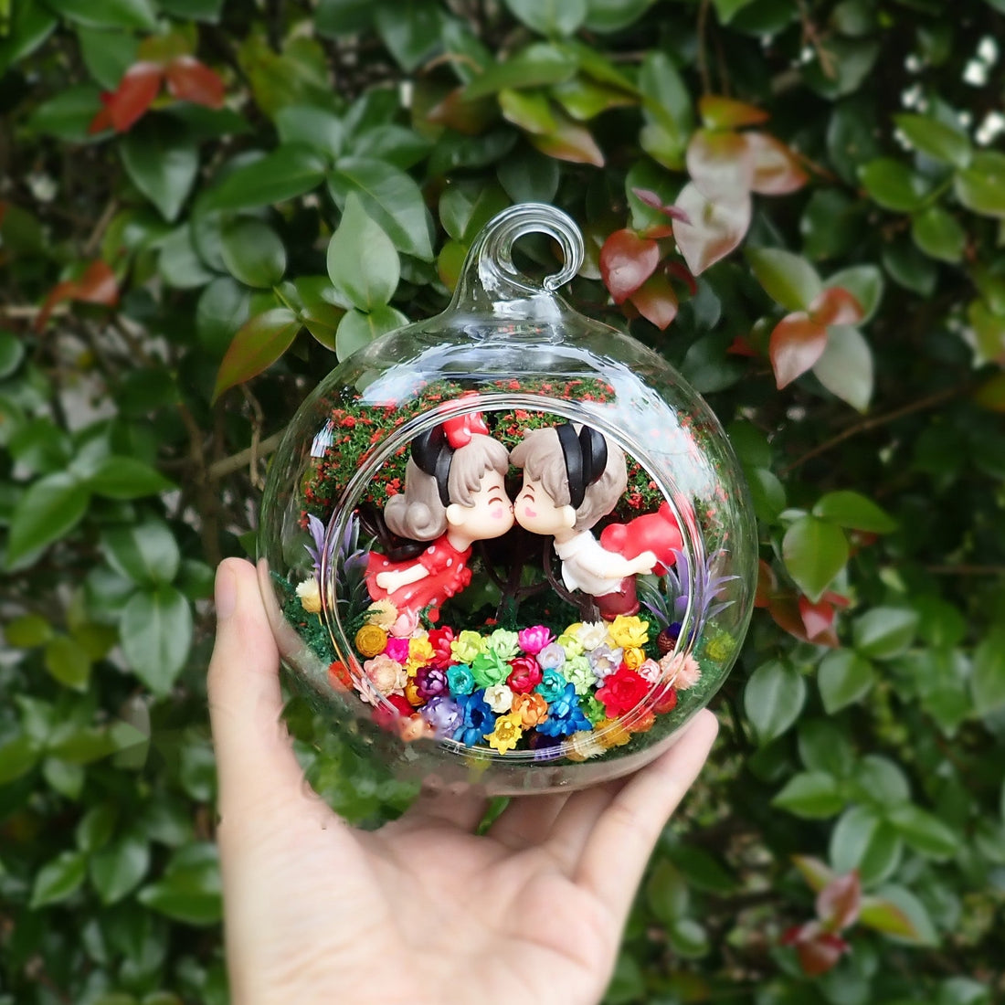 Terrarium kaca bulat dengan patung pasangan tikus di antara bunga awet