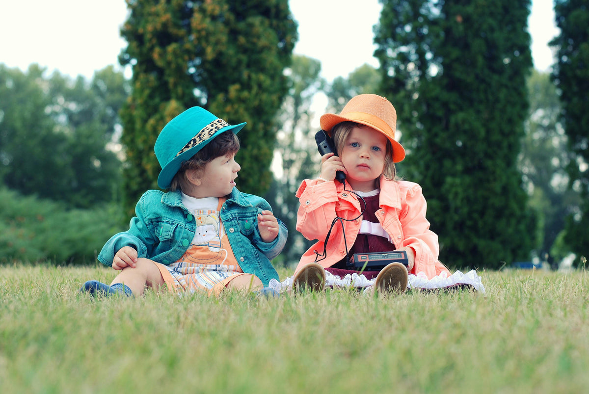 Two toddlers in colourful hats playing on the grass