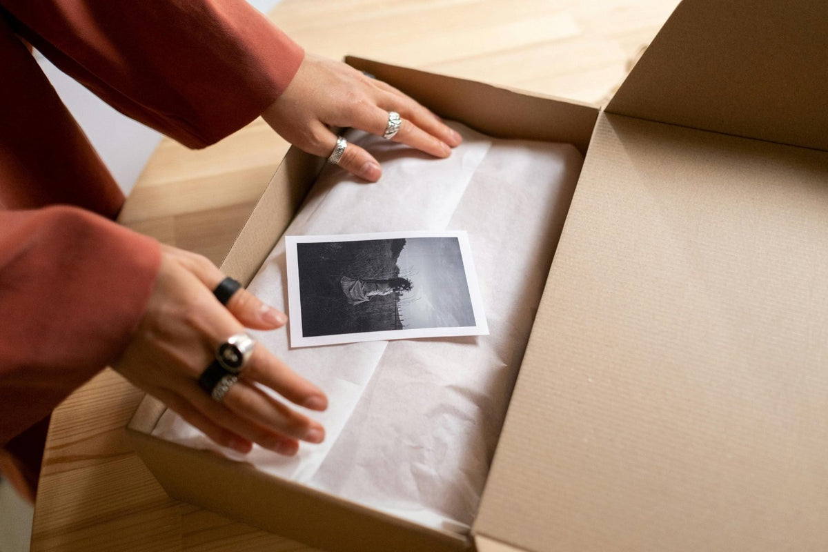 Hands packing a gift box with tissue paper and a photo