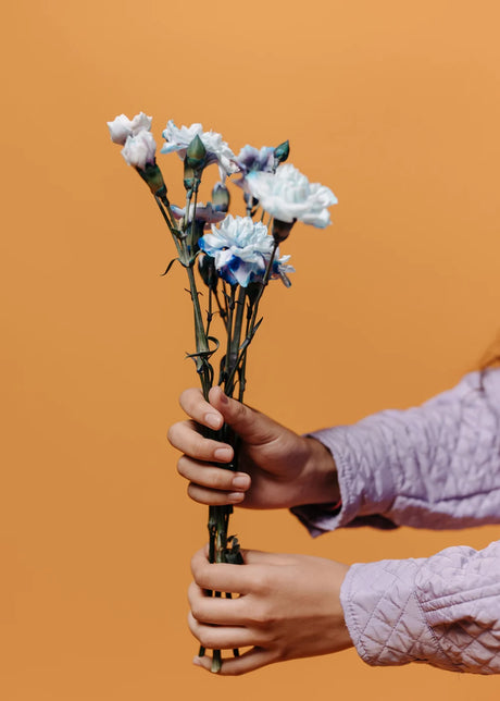 Hands passing a flower bouquet on a peach background
