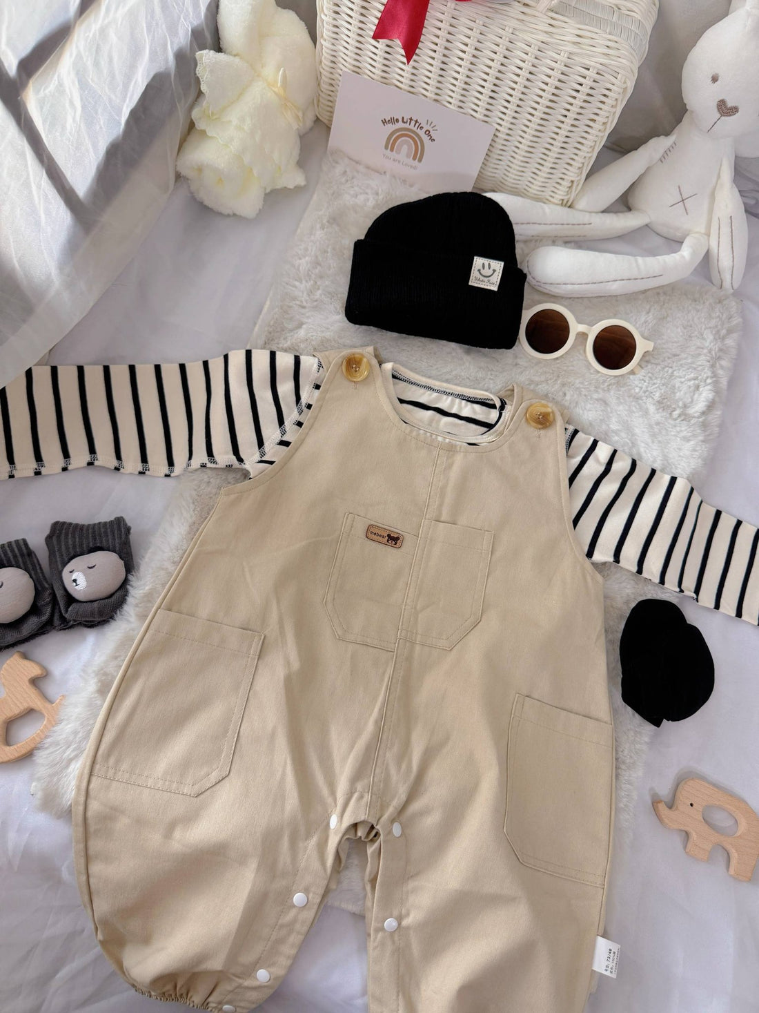 Tiny Trendsetter baby outfit flat lay – khaki overalls with striped top and black beanie