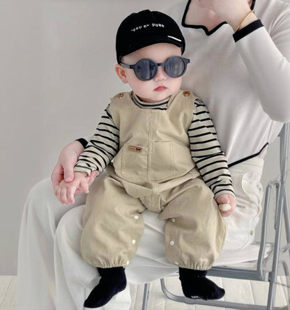 Baby wearing the Tiny Trendsetter khaki overalls with striped top and black beanie