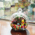 Terrarium kaca bulat dengan patung beruang kuning di antara bunga awet